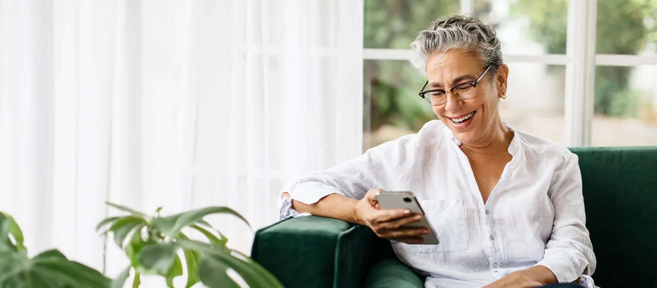 Ältere Frau mit Brille schaut lächelnd auf ihr Smartphone